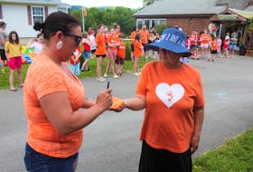 Felicia Paul, left, paints her mother-in-law Shirley Christmas' hand with orange paint so the residential school survivor can make the first hand print on the memorial fence at Kluscap Ridge RV and Campground on Friday. NICOLE SULLIVAN/CAPE BRETON POST