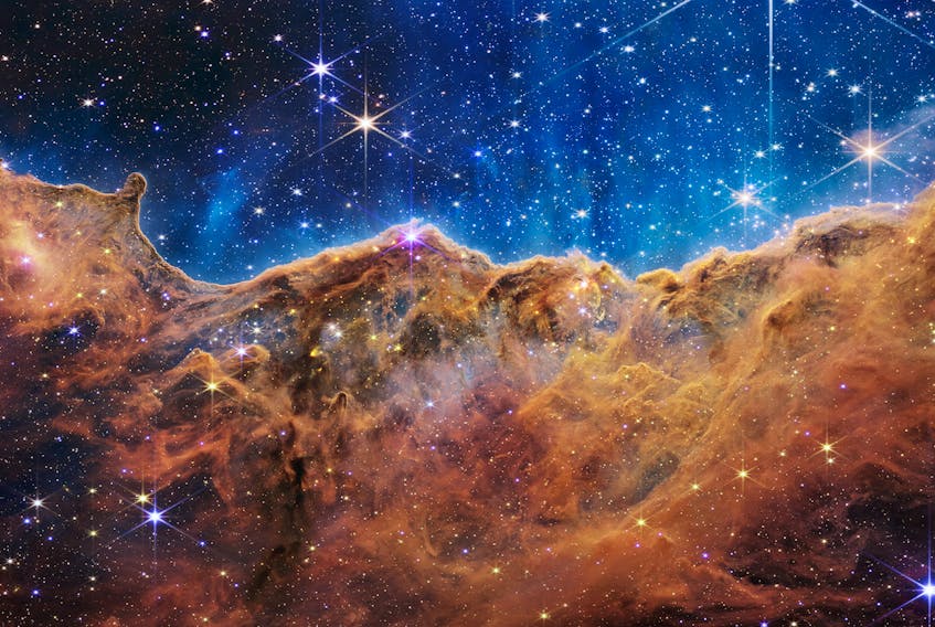 The "Cosmic Cliffs" of the Carina Nebula is seen in an image divided horizontally by an undulating line between a cloudscape forming a nebula along the bottom portion and a comparatively clear upper portion, with data from NASA's James Webb Space Telescope, a revolutionary apparatus designed to peer through the cosmos to the dawn of the universe and released July 12, 2022. Speckled across both portions is a starfield, showing innumerable stars of many sizes. NASA, ESA, CSA, STScI, Webb ERO Production Team/Handout via REUTERS