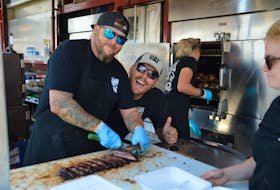 Ryan Durnford, left, cuts a slab of ribs at Billy Bones BBQ while owner Andrew Reinhart sneaks in to give a thumbs up. Billy Bones was one of four ribbers vying for the title of best ribber at the Sydney RibFest 2022, a title Reinhart said they've nabbed seven out of eight times here. NICOLE SULLIVAN/CAPE BRETON POST