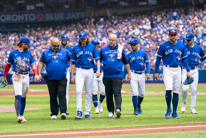 Blue Jays starter Kevin Gausman, third from left, is brought off the field with trainers and players after being hit by a ball in the ankle against the Rays in the second inning of the first game of a doubleheader at the Rogers Centre in Toronto, Saturday, July 2, 2022.