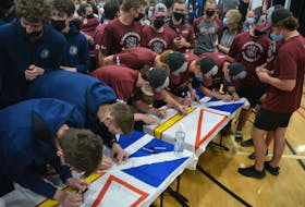 Members of the 2022 Newfoundland and Labrador Canada Games team sign a pair of provincial flags during a rally at the Newfoundland and Labrador Sports Centre on July 19. Nicholas Mercer/The Telegram