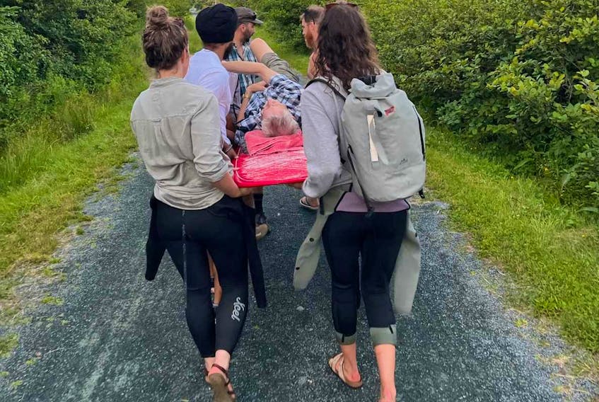 Surfers carry injured cyclist Marcel Maessen to safety after he crashed on the Atlantic View Trail near Lawrencetown Beach on July 22.