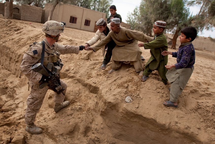 FILE PHOTO: U.S. Marine LCpl Owen Selby, attached to the 2nd Battalion 2nd Marines from Camp Lejeune, North Carolina, hands candy to local Afghan boys while keeping guard over a shura, or meeting of leaders, in the Garmsir district of Helmand Province on December 21, 2009.   REUTERS/Adrees Latif/File Photo  U.S. Marine LCpl Owen Selby, attached to the 2nd Battalion 2nd Marines from Camp Lejeune, N.C., hands candy to local Afghan boys while keeping guard over a shura, or meeting of leaders, in the Garmsir district of Helmand Province on Dec. 21, 2009. The United States and other allies left Afghanistan one year ago after a 20-year war precipitated by the 9/11 terrorist attacks. REUTERS file photo/Adrees Latif