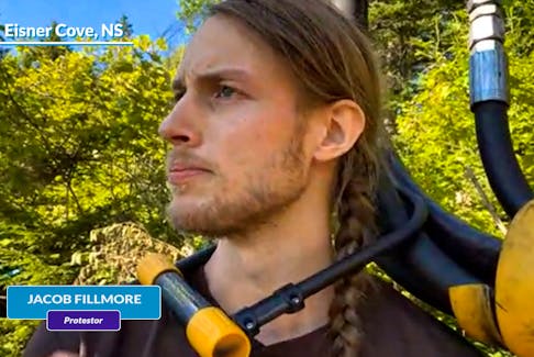 Jacob Fillmore has a bicycle lock around his neck, attached to a piece of forestry equipment in Dartmouth.