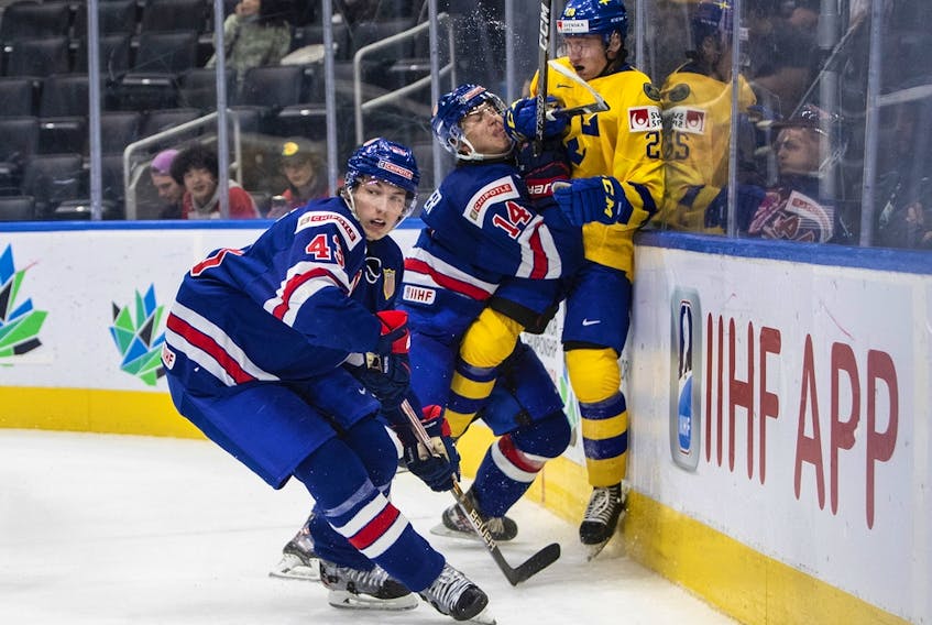 USA's Brock Faber (14) checks Sweden's Oskar Magnusson (28) as Luke Hughes (43) looks for the puck during third period IIHF World Junior Hockey Championship action in Edmonton on Sunday August 14, 2022.