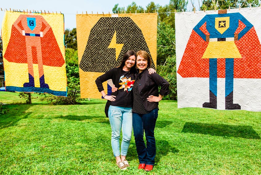 Nicole Forgeron-MacArthur, let, and Carolyn Guy stand in front of the three different styles of Caleb's Superhero Quilts being donated to children with critical illnesses. CONTRIBUTED/MICHELLE LEUDY