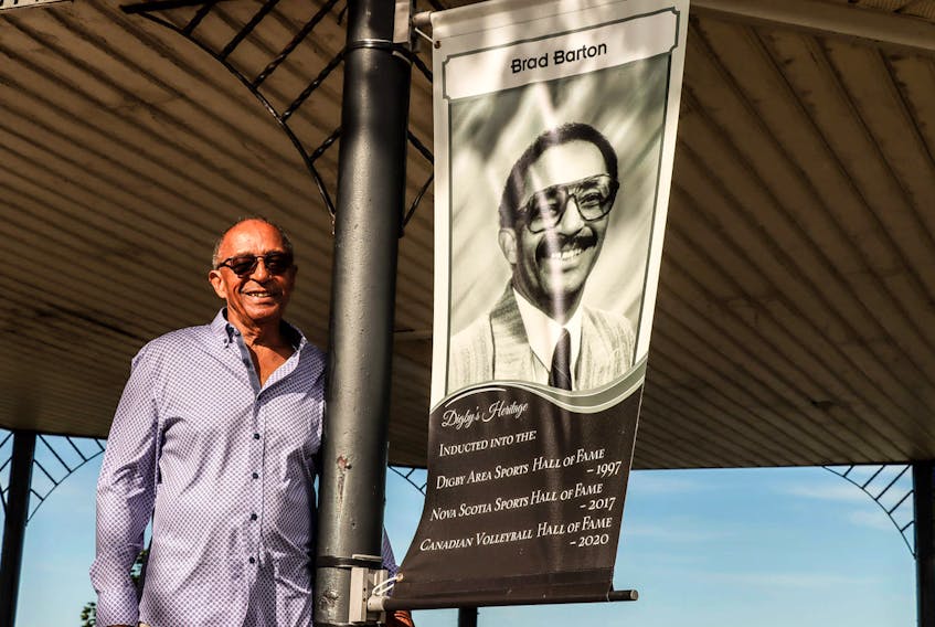 Brad Barton stands beside the new banner in the Town of Digby that honours his 50 year career as a volleyball official, administrator, and builder.  Contributed

