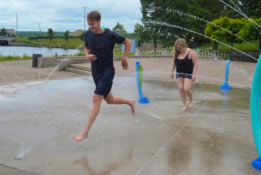 Daniel Bowles, front, and Samantha Mann run through the sprinkles at Wentworth Park in Sydney on July 22 to cool off during the heat wave. NICOLE SULLIVAN / CAPE BRETON POST  xxx