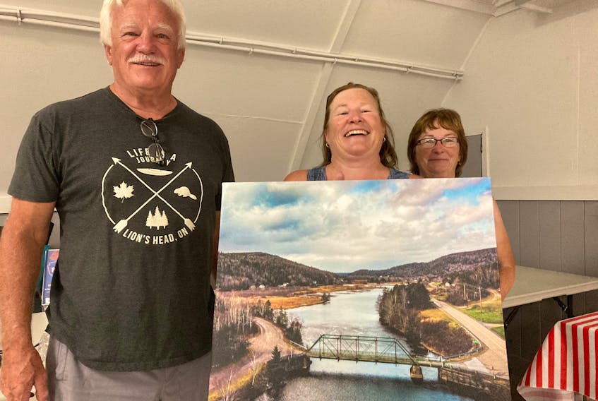 Dave Mansfield, Samantha Dort and Theresa Beiswanger prepare the Country Harbour Gun Club for family movie night. They are holding picture of the 'Iron Bridge' that joins the two sides of the community.