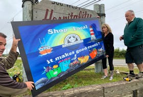 Stacey Stoddard (from left), Anne Lovitt and Carl Dixon install one of the new signs in the Barrington Passage business district near the Cape Sable Island Causeway promoting shopping locally. The sign was commissioned by the  Barrington & Area Chamber of Commerce and painted by Lovitt. KATHY JOHNSON