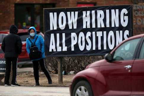People standing near a sign indicating that a local business is hiring in Winnipeg.