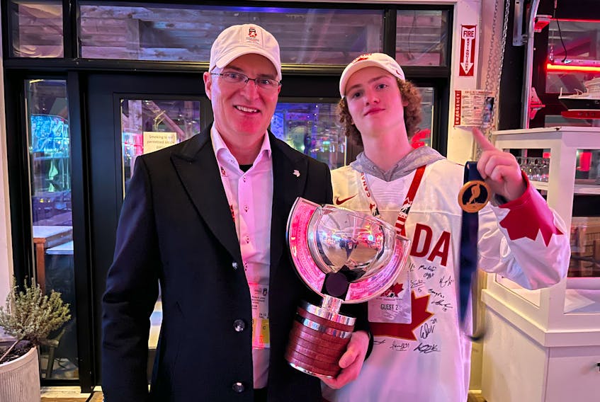 Dr. R.J. MacKenzie of Albert Bridge, left, holds the 2023 IIHF World Junior Hockey Championship trophy along with his youngest son Braedy after Team Canada won the gold medal in Halifax last Thursday. CONTRIBUTED/R.J. MACKENZIE