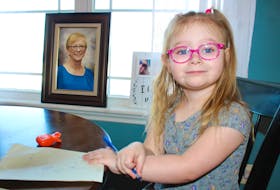 Nora Snow, 3, sits at the dining room table at her Donkin home in front of a photo of her grandmother Charlene Snow, who she loved shopping with. Pen in hand, Nora plans on "doing work for Nan, too" like her mother Katherine Snow who has started a website to publish stories about Nova Scotia's healthcare system failing patients like Charlene. NICOLE SULLIVAN/CAPE BRETON POST