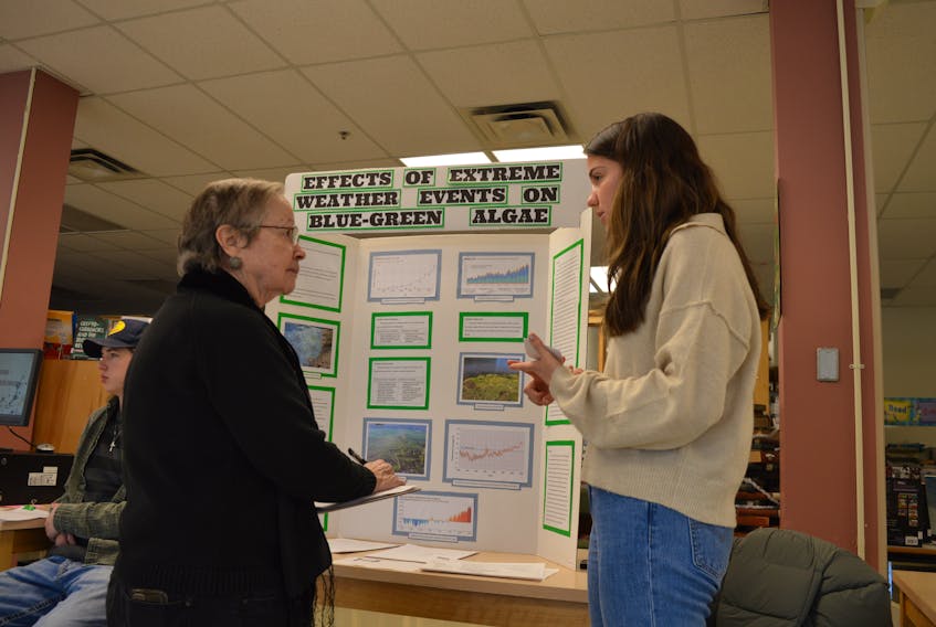 Sadie Parnbaby, right, prepared a presentation on the effects of extreme weather events on blue-green algae for Thursday’s science fair at Sydney Academy. She’s shown explaining her findings to Kelly Donovan, one of three judges for the competition. GREG MCNEIL/CAPE BRETON POST