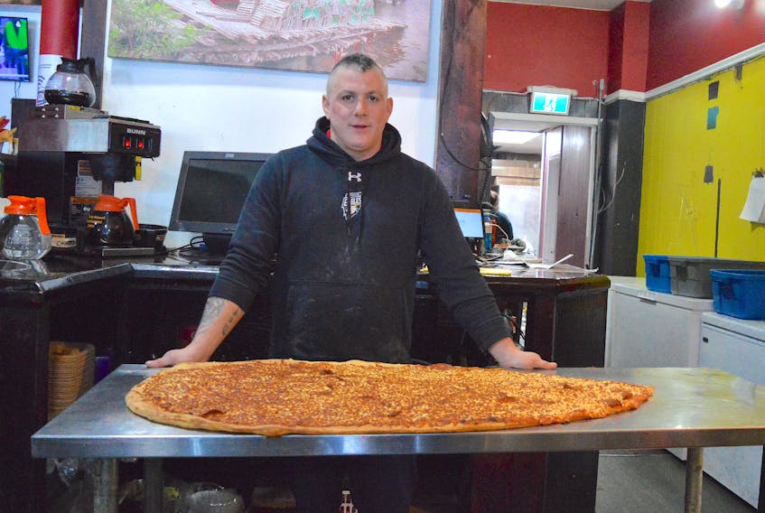 Justin Ayre, owner of four Alexandra's Pizza locations in Cape Breton, shows off the latest eating challenge at the Charlotte Street shop — a giant slice of pizza that measures four-and-a-half feet and weighs a whopping eight pounds. Chris Connors/Cape Breton Post