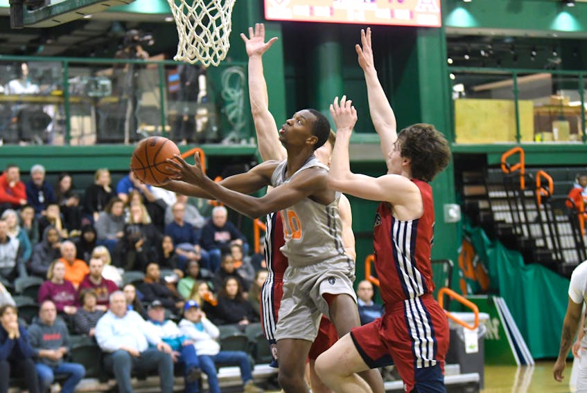 Ceejay Hanson of the Cape Breton Capers, middle, goes for a lay-up during Atlantic University Sport basketball action against the Acadia Axemen at Sullivan Field House in Sydney on Friday. Cape Breton won the game 96-79. PHOTO/VAUGHAN MERCHANT, CBU ATHLETICS.