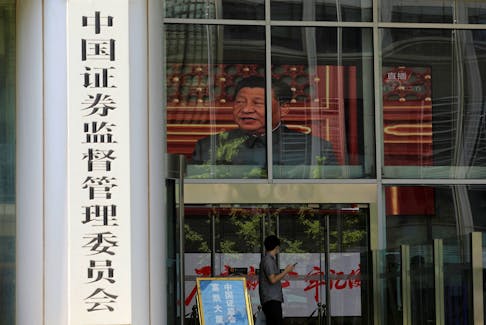 FILE PHOTO: A man stands near a screen showing news footage of Chinese President Xi Jinping at the China Securities Regulatory Commission (CSRC) building on the Financial Street in Beijing, China July 9, 2021. REUTERS/Tingshu Wang/File Photo