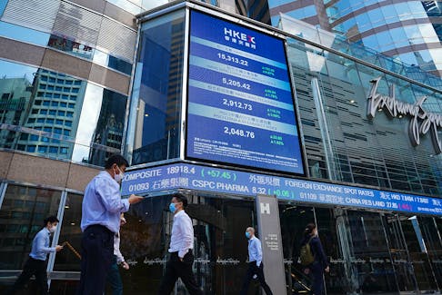 People walk past a screen displaying the Hang Seng stock index at Central district, in Hong Kong, China October 25, 2022.