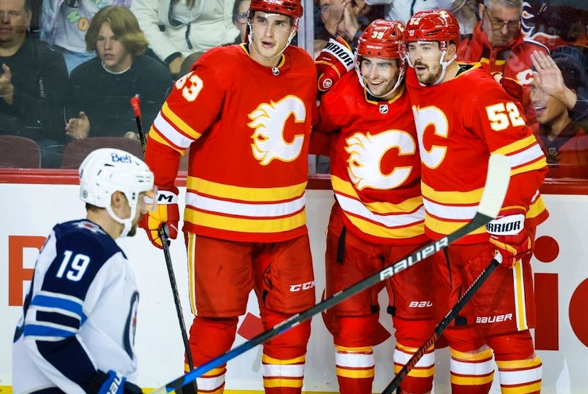 Calgary Flames forward Matthew Coronato, centre right, celebrates his goal with Adam Ruzicka, centre left, and MacKenzie Weegar as the Winnipeg Jets’ David Gustafsson skates past at Scotiabank Saddledome in Calgary on Monday, Oct. 2, 2023.