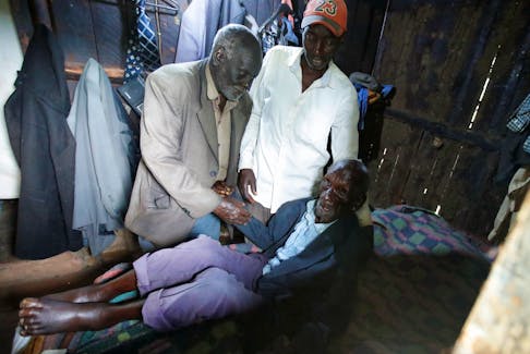 Kibore Cheruiyot Ngasura, 105, a member of the Talai community, which accuses the British colonial government of displacing them from their farms, is assisted to get to bed by his sons, inside his house ahead of Britain's King Charles' and Queen Camilla's visit to Kenya, in Tugunon village of Kericho County, Kenya October 25, 2023.