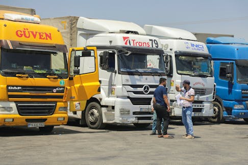 People stand near trucks parked at Bab al-Salameh border crossing in Aleppo countryside, Syria August 9, 2023.