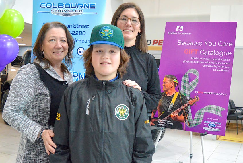 Breton Keeping, centre, the son of the late Cory Keeping, stands next the cover image of the Cape Breton Regional Hospital Foundation’s latest Because You Care Gift Catalogue along with his grandmother Gerry Jessome, left, and mother Nichole Keeping, during a launch event Wednesday at Colbourne Ford in Sydney. Chris Connors/Cape Breton Post