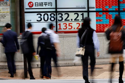 Pedestrians walk past an electronic board displaying Nikkei share average, outside a brokerage in Tokyo, Japan, October 31, 2023.