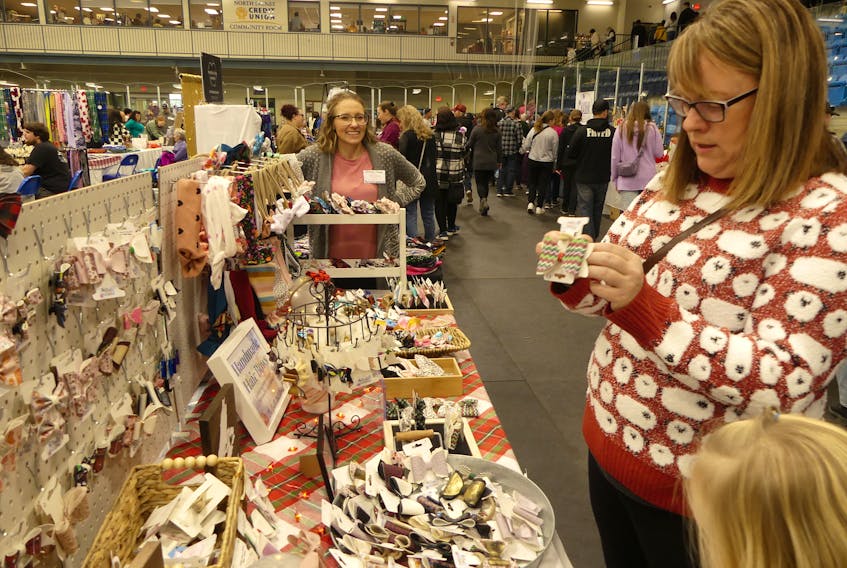 Whitney Mabee, back centre, watches as a customer inspects one of the bows from her booth on Saturday at "The Big One," a large Christmas craft sale held at the Emera Centre Northside in North Sydney. The Big One was one of a handful of holiday craft fairs and sales held in or near Sydney over the weekend, as the holiday shopping season begins to ramp up.