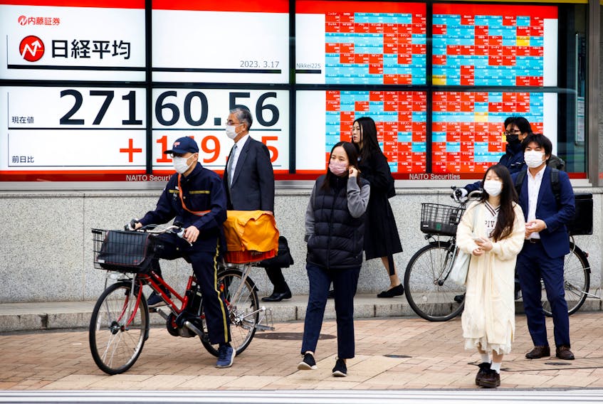 Passersby wait at a crossing in front of an electronic board showing Japan's Nikkei average outside a brokerage, in Tokyo, Japan, March 17, 2023.