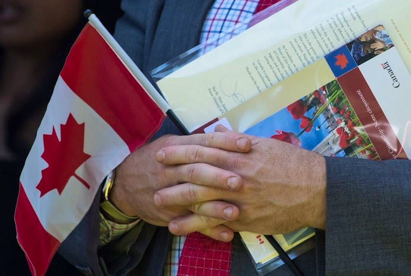 A new Canadian holds a Canadian flag, their citizenship certificate and a letter signed by Prime Minister Justin Trudeau as they sing O Canada after becoming a Canadian citizen, during a special Canada Day citizenship ceremony in West Vancouver on Monday, July 1, 2019. 