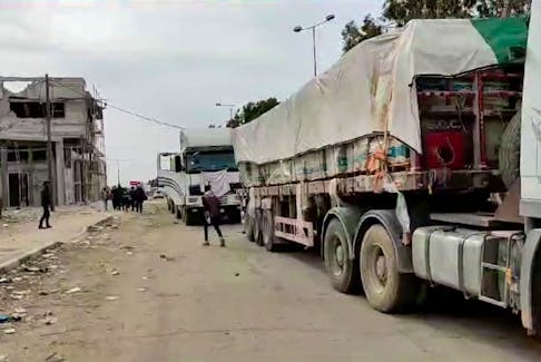 People walk next to trucks with humanitarian aid delivered by the Palestine Red Crescent Society, bound for north Gaza, amid a temporary truce between Israel and the Palestinian Islamist group Hamas, in a location given as Gaza, in this still image obtained from a handout video released November 25, 2023. Palestine Red Crescent Society/Handout via