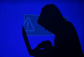 A hooded man holds a laptop computer as blue screen with an exclamation mark is projected on him in this illustration picture taken on May 13, 2017. Capitalizing on spying tools believed to have been developed by the U.S. National Security Agency, hackers staged a cyber assault with a self-spreading malware that has infected tens of thousands of computers in nearly 100 countries.