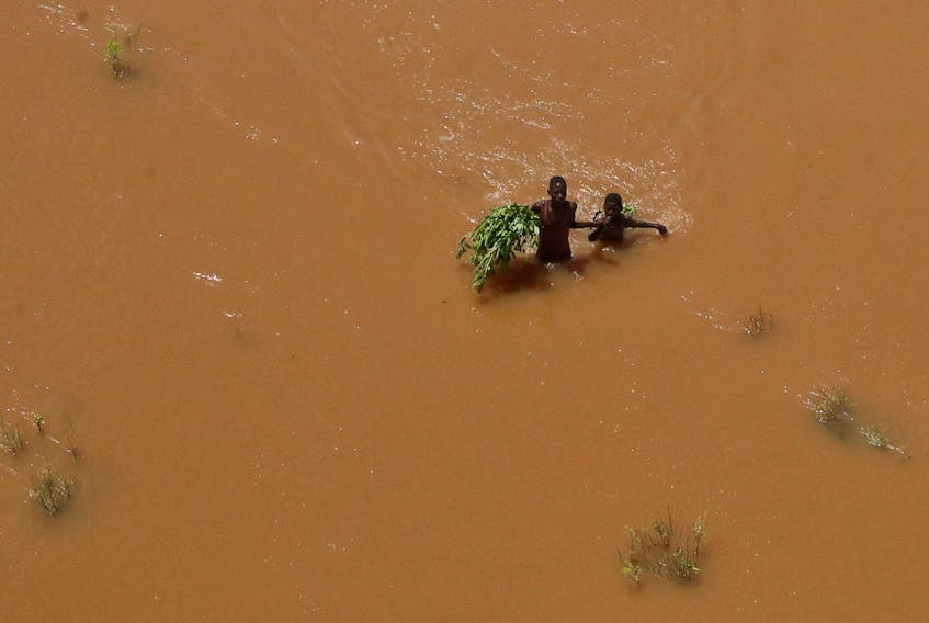 People hold on to plants as they wade through flood waters after they were displaced following heavy rains in Garsen, Tana Delta within Tana River county, Kenya November 23, 2023.
