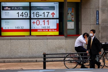 Passersby walk past an electric monitor displaying the Japanese yen exchange rate against the U.S. dollar outside a brokerage in Tokyo, Japan October 4, 2023.