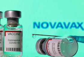 Vials labelled "VACCINE Coronavirus COVID-19" and a syringe are seen in front of a displayed Novavax logo in this illustration taken December 11, 2021.