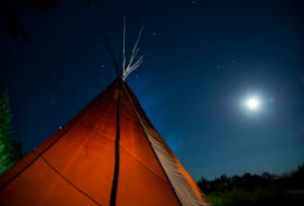 The hunting camp's teepee glows from the light of their fire, under the moonlight of a clear night sky.