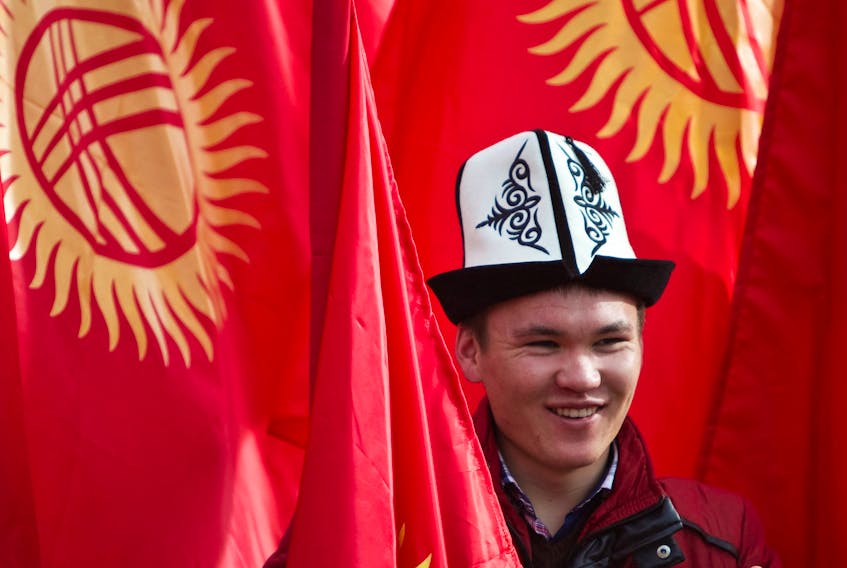 A man wearing a Kyrgyz national hat poses with national flags before a rally marking the Day of Flag and the Day of Kolpak in Bishkek, Kyrgyzstan March 4, 2013.  