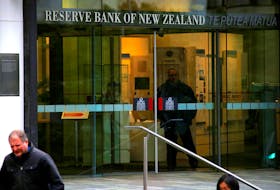 Pedestrians walk past as a security guard stands in the main entrance to the Reserve Bank of New Zealand located in central Wellington, New Zealand, July 3, 2017.