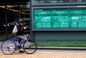 A man on a bicycle stands in front of an electronic board showing Shanghai stock index, Nikkei share price index and  Dow Jones Industrial Average outside a brokerage in Tokyo, Japan September 22, 2022.