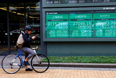 A man on a bicycle stands in front of an electronic board showing Shanghai stock index, Nikkei share price index and  Dow Jones Industrial Average outside a brokerage in Tokyo, Japan September 22, 2022.