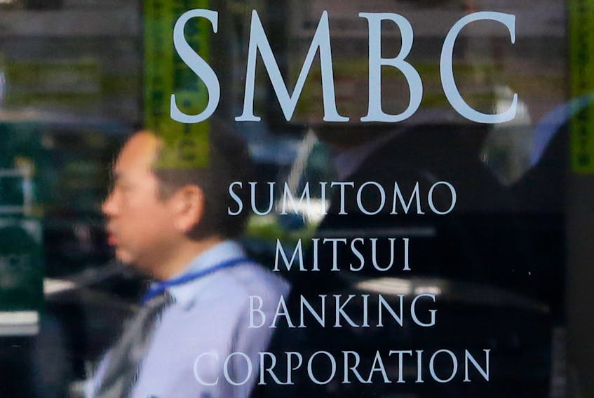 A man is reflected on a sign outside a branch of Sumitomo Mitsui Banking Corporation in Tokyo November 13, 2014.