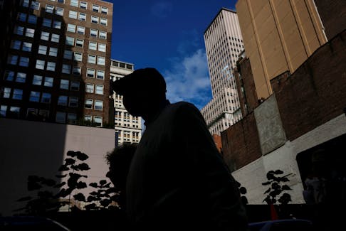A man is seen silhouetted wearing a protective face mask, amid the coronavirus disease (COVID-19) pandemic, walking near the financial district of New York City, U.S., October 18, 2021.