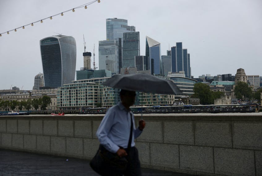 A pedestrian carrying an umbrella walks along the River Thames in view of City of London skyline in London, Britain, July 31, 2023.