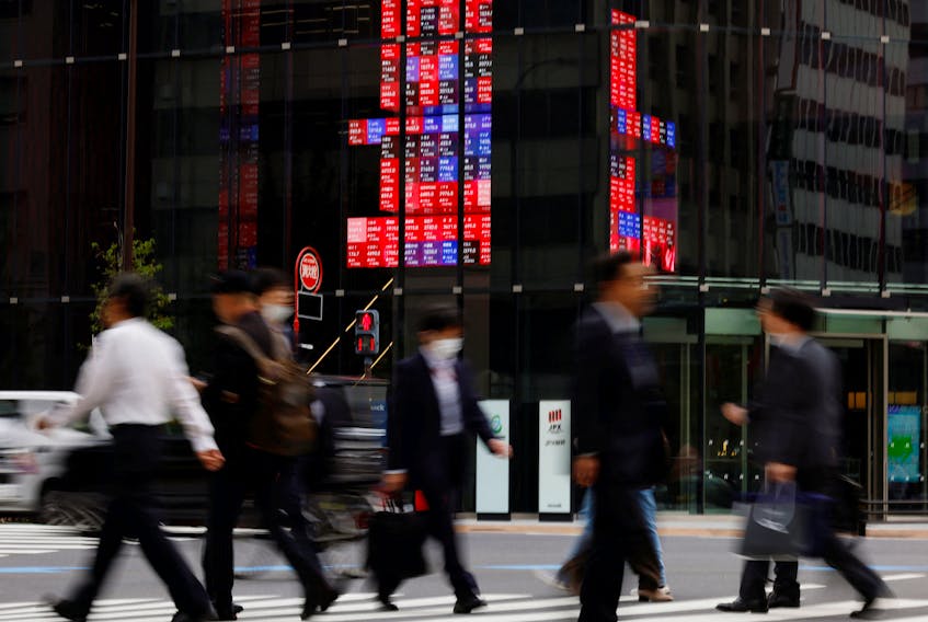 Pedestrians walk past an electronic board displaying various companies' share prices, at a business district in Tokyo, Japan, October 31, 2023.