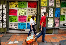 People walk past a grocery with signs announcing prices of food, in Caracas, Venezuela August 25, 2022.