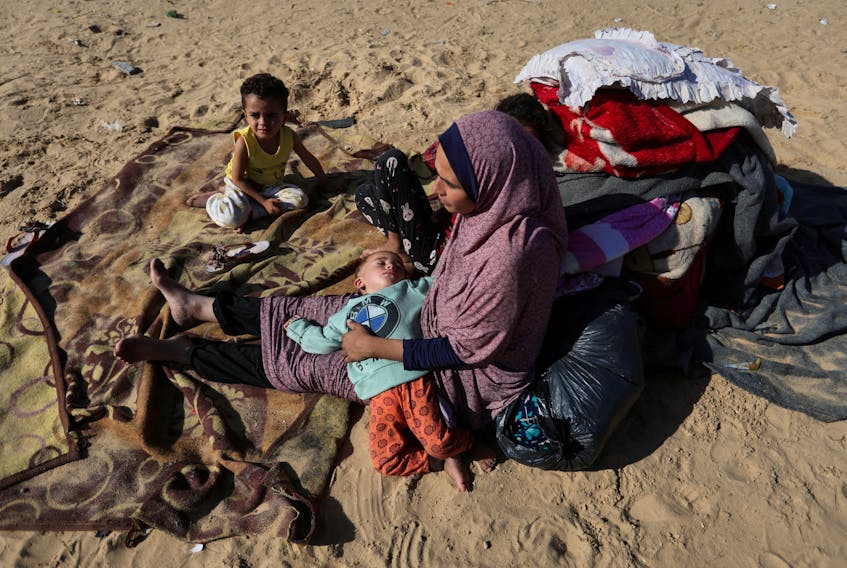 A woman sits with children outside, as displaced Palestinians, who fled their houses due to Israeli strike, shelter in a camp in Rafah, amid the ongoing conflict between Israel and Palestinian Islamist group Hamas, in the southern Gaza Strip, December 6, 2023.