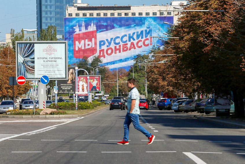 A pedestrian crosses a street near a building with a banner displaying the slogan "We are Russian Donbass!" in the rebel-held city of Donetsk, Ukraine September 9, 2021.