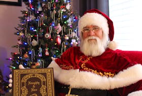 Santa Claus sits in front of his decorated Christmas tree, holding his Naughty and Nice Book as he prepares for the festive season. - Cameron Kilfoy/The Telegram