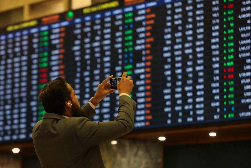 A man uses a mobile phone as he takes a photo of the electronic board displaying share prices during a trading session at the Pakistan Stock Exchange, in Karachi, Pakistan November 28, 2023.
