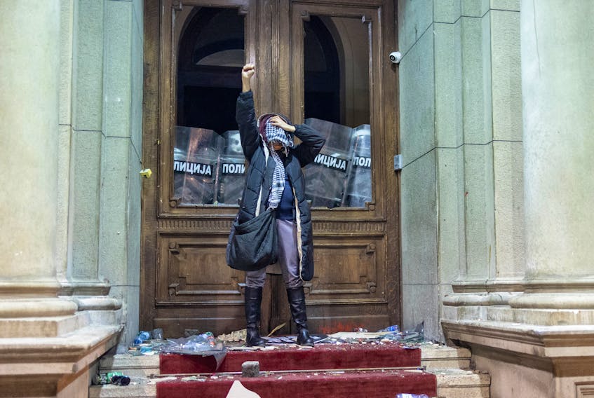 A protester raises her fist as police officers guard the door of the city hall during a protest by supporters of the opposition 'Serbia Against Violence' (SPN), after the SPN alleged major election law violations in the Belgrade city and parliament races, in Belgrade, Serbia, December 24, 2023.